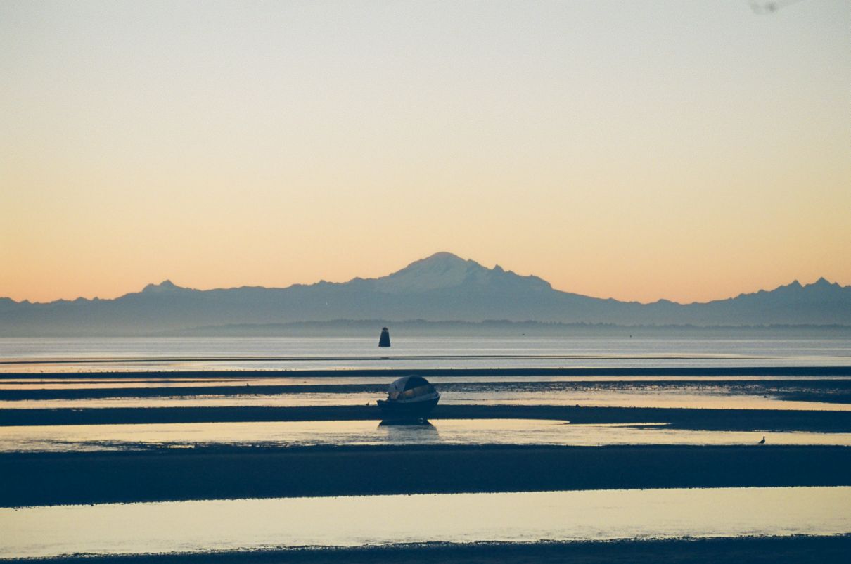 sun rises behind mountain in background, boat leaning on sandbar in foreground
